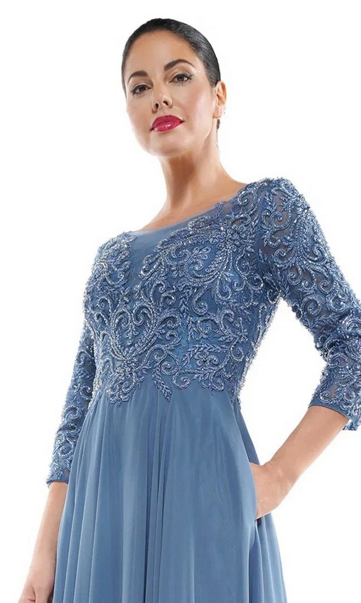 A woman models the Marsoni MV1052 Long Formal Dress, featuring a blue beaded bodice, sheer sleeves, and an elegant chiffon A-line skirt, set against a white background.